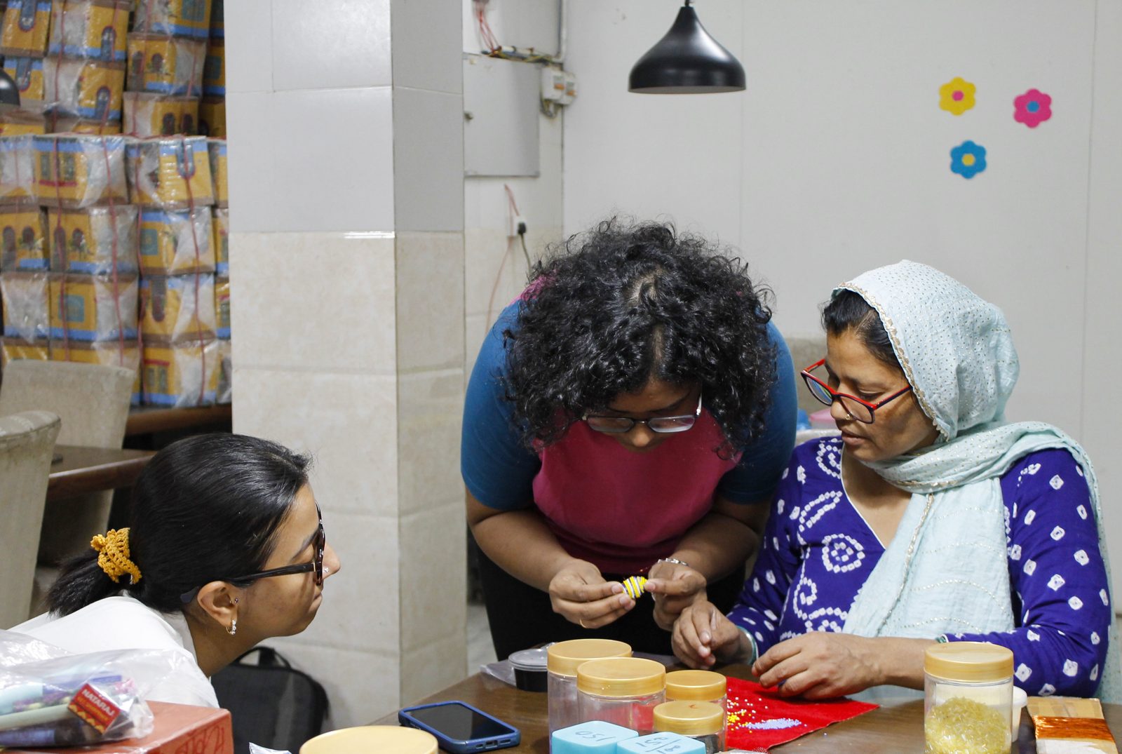 Three women beading at a workshop table covered with sketches and colour references