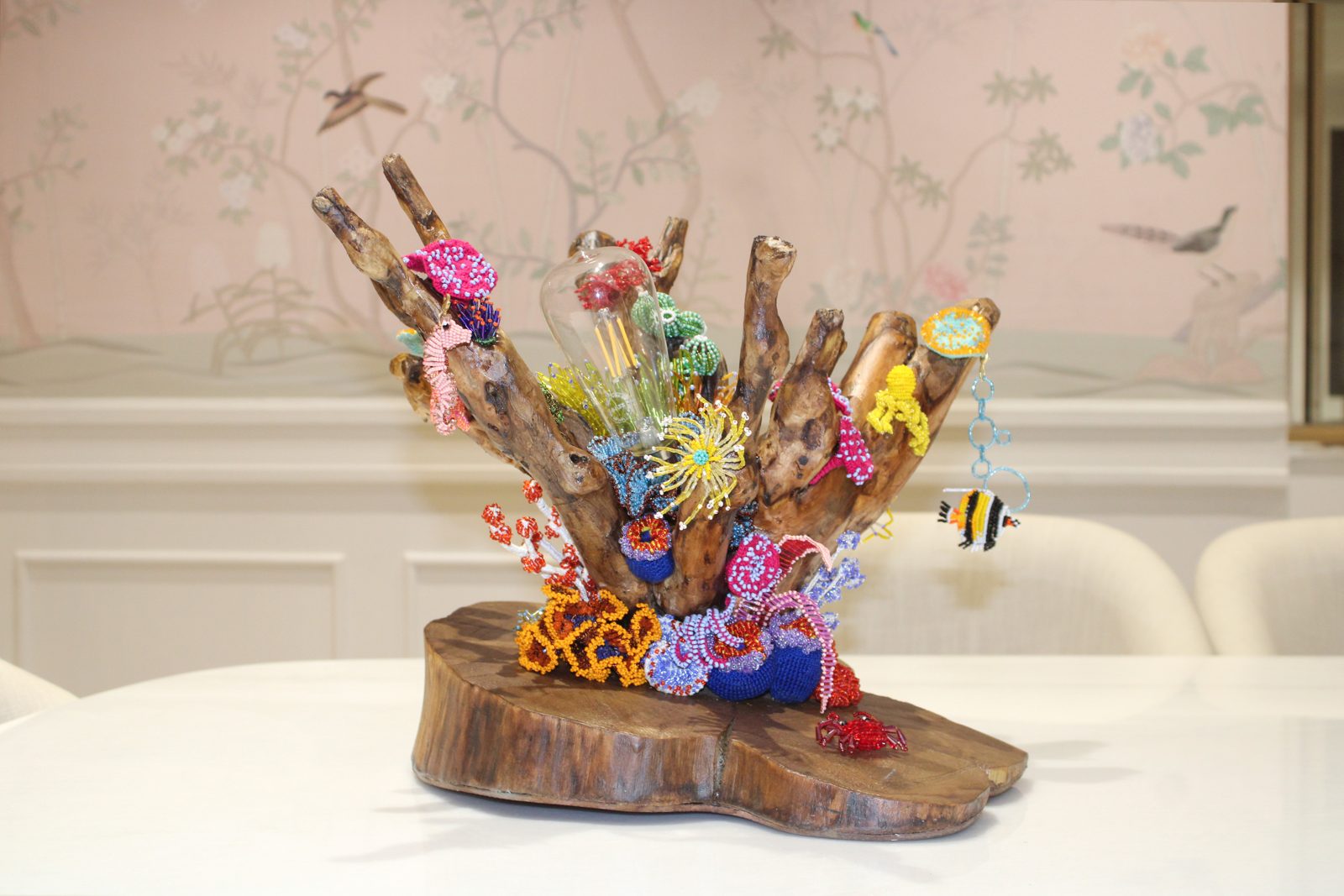 A cluster of beaded coral forms in pink, yellow and blue growing out of a piece of driftwood