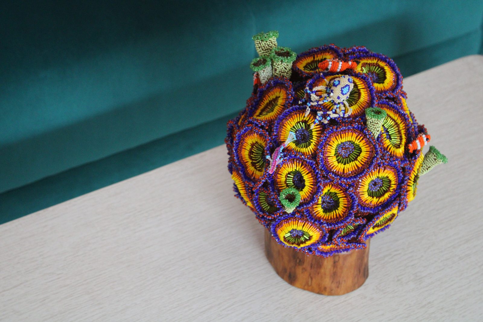 A sphere covered in beaded zoanthid forms in purple and yellow on a wooden base, on a carpet