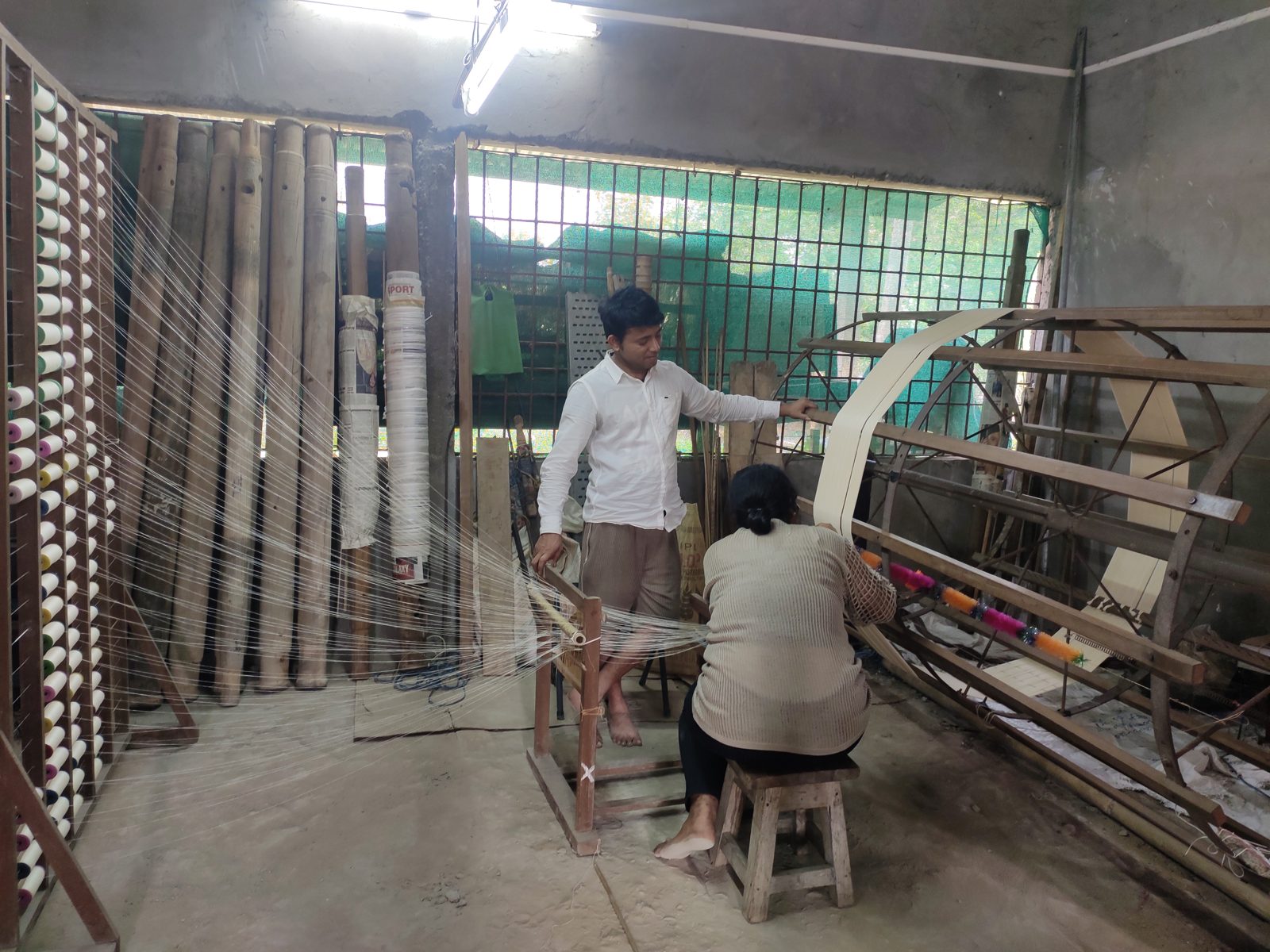Two weavers at a large wooden handloom in a workshop