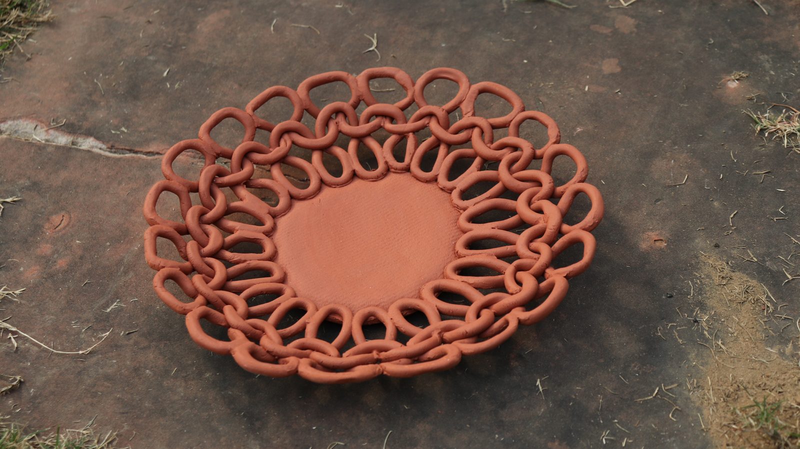 A round plate made of interlocking terracotta rings, on grass