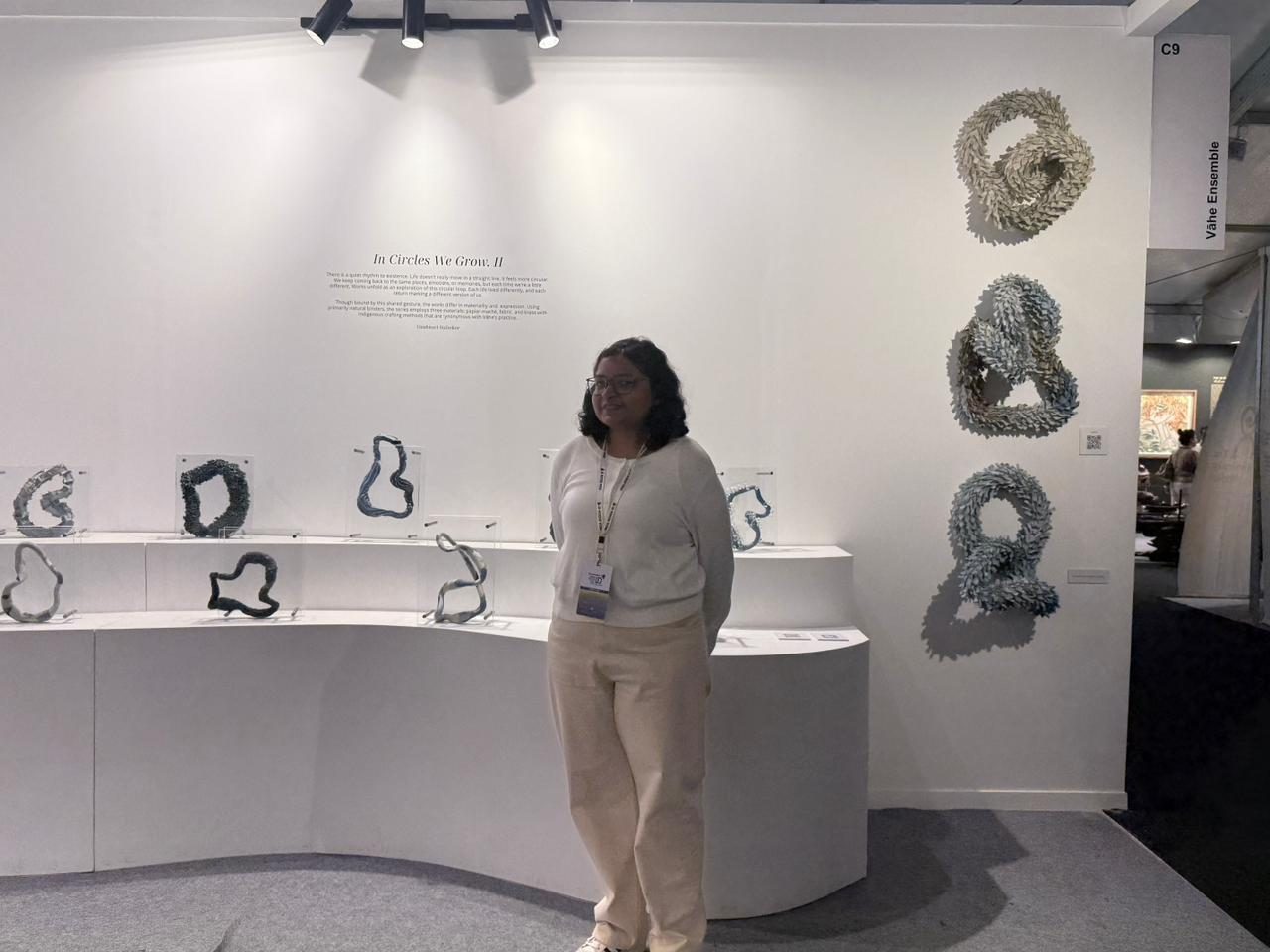 Yashica standing in a white exhibition booth beside a wall of looped, organic sculptural forms